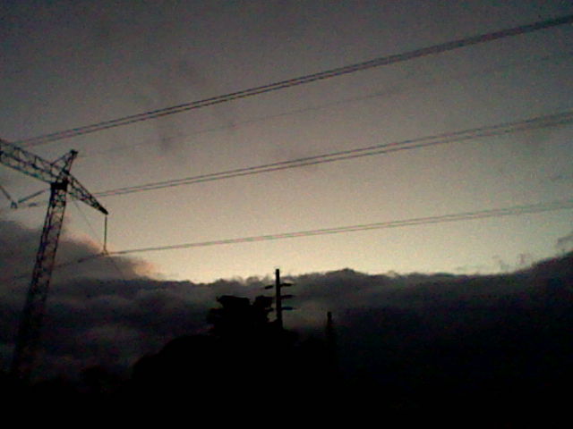 Another sundown. Electricity lines go horizontally across the image. The bottom of the image has more clouds, and the sky has a gradient going from bright unsaturated pink at the bottom to grey at the top.