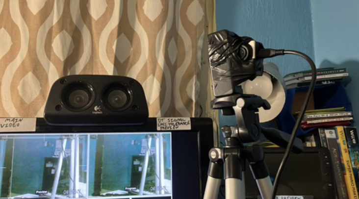 A camera jerry rigged onto a tripod phone mount. To the left of the camera is a monitor displaying the video feed of the camera.