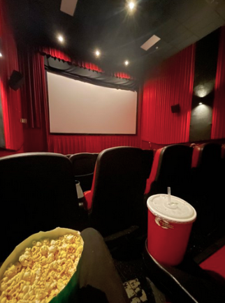 An image of a movie theater. At the bottom of the image is a big bag of popcorn and a big red soda cup.