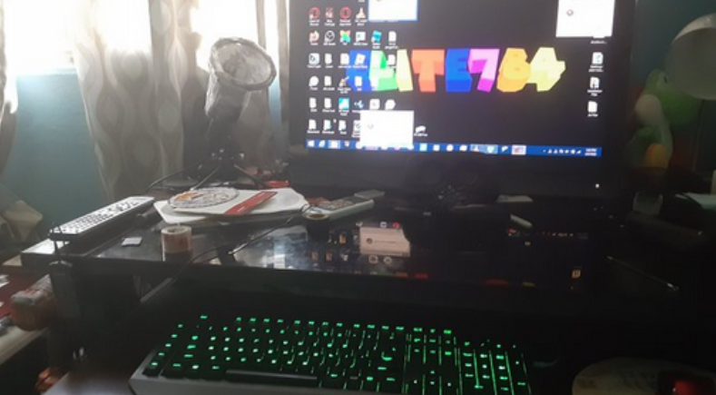 Image of a table. There is a VIZIO television at the back, and on the under table of the table is a keyboard with a green backlight and a red mouse.